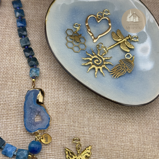 Detail of the Blue Portal™ gemstone necklace with blue agate stones and slice with a gold detachable butterfly charm and a Resist2it charm, next to other detachable charms
