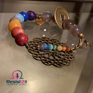 Chakra Explosion colorful bracelet reflected on glass surface in warm ambient lighting, featuring the Resist2it brand