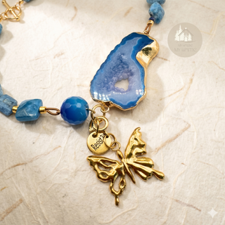 Detail of the Blue Portal™ gemstone necklace with blue agate stones and slice with a gold detachable butterfly charm and a Resist2it charm