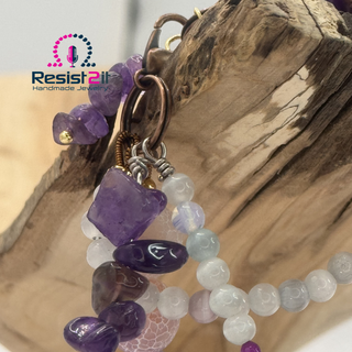 Mixed Feelings™ bracelet styled flat lay showing purple jasper, agate, and bead combination on a wooden piece of art — Jewelry by Jules, featuring the Resist2it brand logo