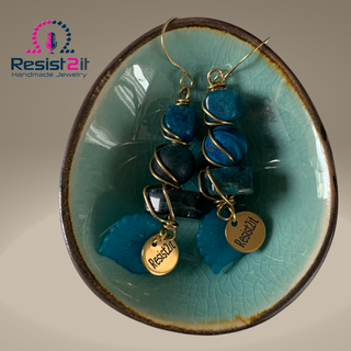 Handmade blue earrings in ceramic bowl flat lay luxury product styling with Resist2it logo
