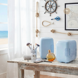 Two light blue mini FRESCA™ fridges on a wooden table with beach decor in the background.