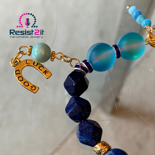 Necklace with blue and gold beads and a 'Good Luck' charm on a white background.
