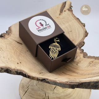 Gold Jules' Cute Jellyfish Charm™ in a brown giftbox on a wooden surface with 'Resist2it' branding