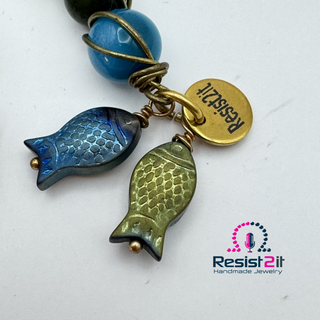 Detail of the blue and green fish charms of the Hooked!™ handmade earrings by Resist2it