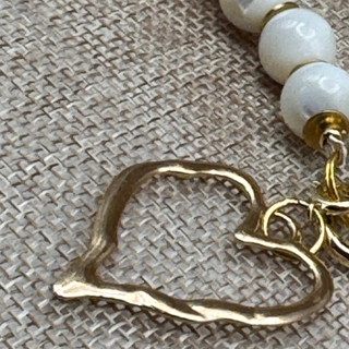 Detachable gold heart-shaped charm JULES' BIG HEART™ on necklace with white beads