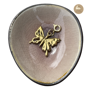 Gold butterfly charm on a textured ceramic dish