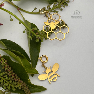 Jules' Golden Bee™ charm and Jules' Hive™ charm on green leaves