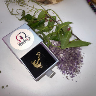 Jules’ Inner Orbit Charm™ in a box with purple crystals and green leaves on a white background