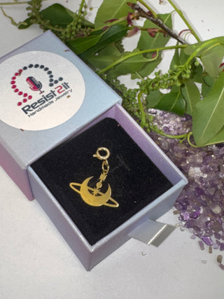 Jules' Inner Orbit Gold charm in a Resist2it giftbox with green leaves and crystals in the background