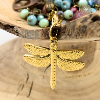 Gold Jules' Magical Dragonfly charm on a wooden surface with colorful beads in the background