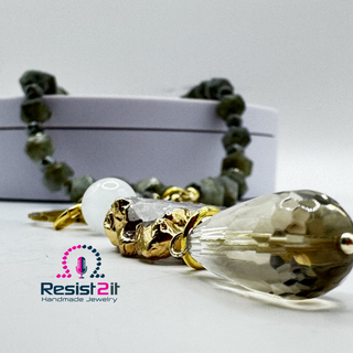 Handmade jewelry with gold and crystal elements on a white surface, featuring the Resist2it brand, showing detail of a faceted smoky quartz bead.