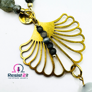 Detail of a golden flower pendant with little grey moonstones on it and a charm of the Resist2it brand.