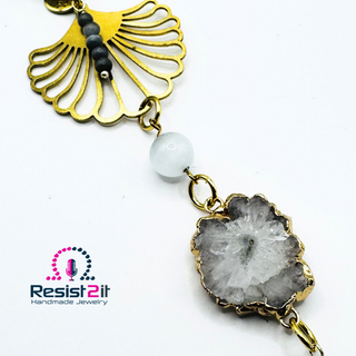 Detail of a handcrafted necklace with delicate flower connector and natural gemstone white crystal pendant on a white background, featuring the Resist2it brand.