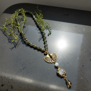 LABRADORITE MOONLIGHT™ necklace with faceted labradorite beads and gold shell pendant on a reflective surface