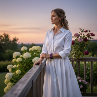 Woman in a white dress standing on a balcony wearing Mystical Nights purple stone bead bracelet 