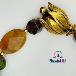 Detail of a statement bracelet with peridot gemstones and sea sediment stoneJewelry with gold and brown beads, and a golden tulip, featuring the Resist2it logo.