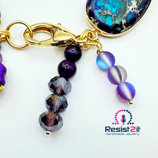 PURPLE TIDES™  charms with purple faceted beads, amethist and cat's eye beads and gold-filled lobster clasp, featuring 'Resist2it Handmade Jewelry' logo.
