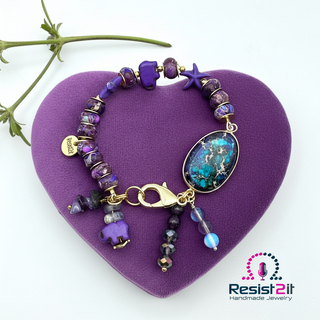 PURPLE TIDES™ beaded artisanal bracelet with a purple gemstones and starfish charms by Resist2it on a purple heart-shaped pillow