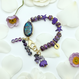 Purple Tides beaded bracelet with gold accents on a white floral background