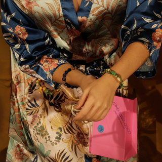 Person wearing floral-patterned clothing with a pink bag and handmade bracelets by Resist2it.