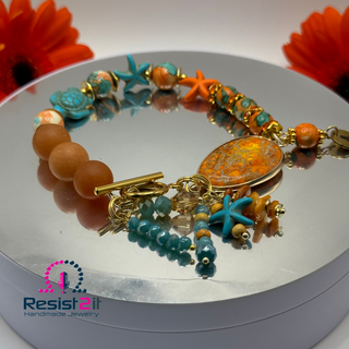 TURANCIA™ handmade bracelet displayed with orange flowers highlighting ocean and coral colors.