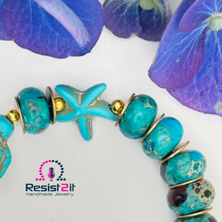 Artisanal turquoise beaded bracelet with starfish and golden findings on a white background with purple flowers.