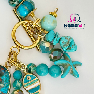 Turquoise beaded handmade bracelet with gold accents and starfish and fish charm on a white background, featuring Resist2it logo.