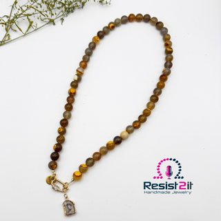 UNSPOKEN™ Tiger Skin Agate beaded necklace with a pendant on a white background, featuring the Resist2it brand.
