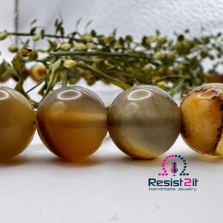 Four brown and beige beads of the UNSPOKEN™ necklace made of Tiger Skin Agate, featuring the Resist2it logo
