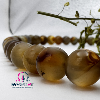 Close-up of Unspoken™ Tiger Skin Agate beads with their soft translucency, featuring the Resist2it Handmade Jewelry logo