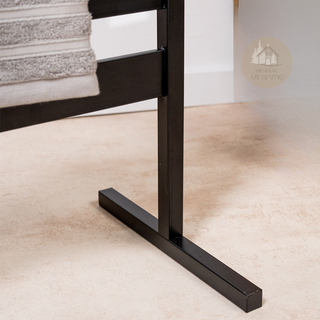 Close-up of a black metal chair leg of the standing White towel on the Black AUREA™ Electric Heated Towel Rail on a beige bathroom floor.