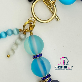 Beaded keychain with blue and gold elements on a white background, featuring Resist2it Handmade Jewelry logo.