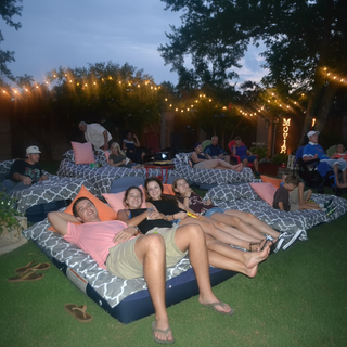 People relaxing on outdoor lounge chairs under string lights at night.