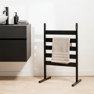Black AUREA™ Electric Heated Towel Rail – 5 Bars standing with a beige towel in a bathroom setting